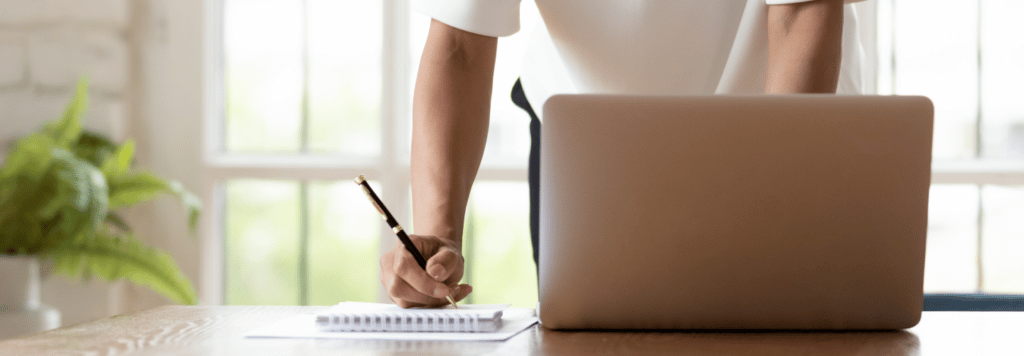 Person taking notes beside a laptop